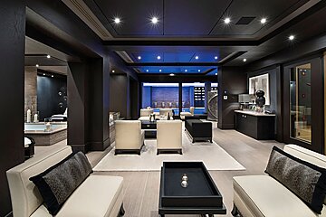 A modern, dark-toned luxury spa and lounge area with cream furniture, blue accent lighting, and a hot tub.