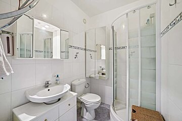 A clean, brightly lit white bathroom with a sink, toilet, curved shower cabin, and mirrored cabinets. Blue accent tiles are visible.