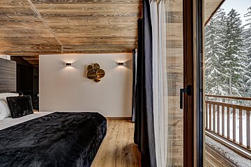 A bedroom with a bed and a balcony with trees in the background