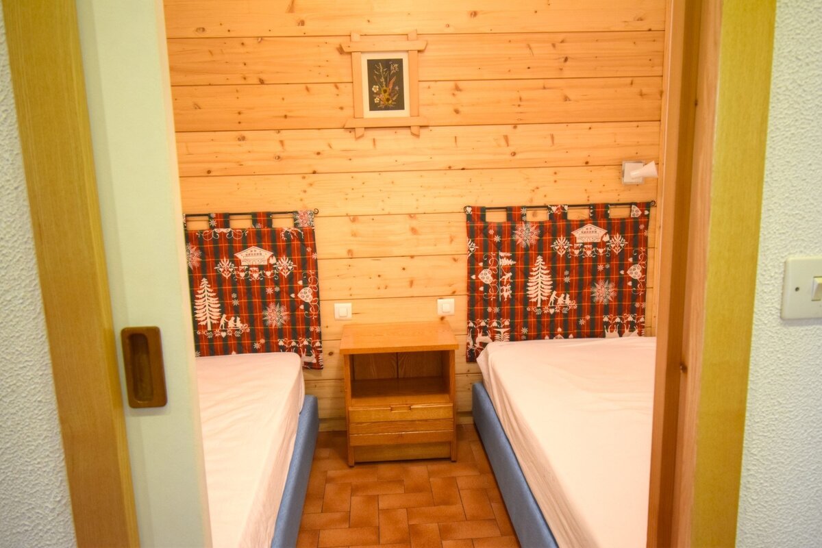 A cozy wood-paneled bedroom featuring two twin beds with red festive headboards and a nightstand in between.