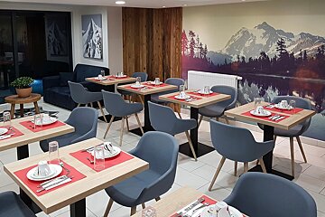 A dining room with tables and chairs and a painting of mountains on the wall