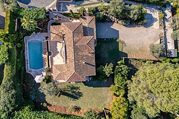 Aerial view of a luxurious villa with a terracotta roof, a sparkling swimming pool, lush green landscaping, and a gravel driveway.