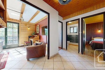 Rustic hallway with tiled floor leading to a sunny living room, a bathroom, and a bedroom in a cozy cabin.