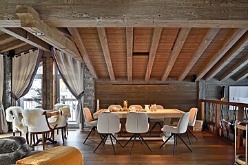 Luxurious wooden cabin interior featuring a rustic dining table with modern chairs under a vaulted ceiling with exposed beams.