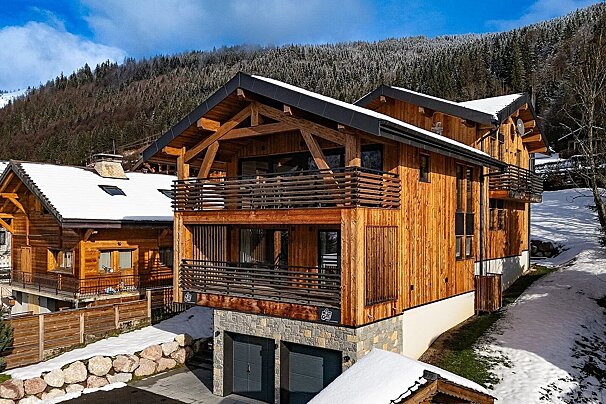 A modern wooden alpine chalet with balconies on a snow-covered mountain slope.