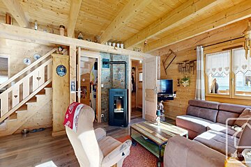 Rustic wooden cabin interior featuring a cozy living room with a brown sofa, a wood-burning stove, and a staircase.