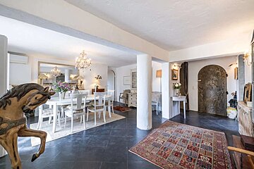 An eclectic interior features a white dining area with a chandelier, dark tiled floor, an ornate arched doorway, and a decorative rocking horse.