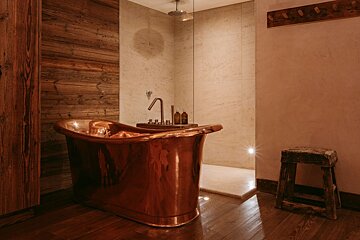 A bathroom with a copper bathtub and a wooden stool