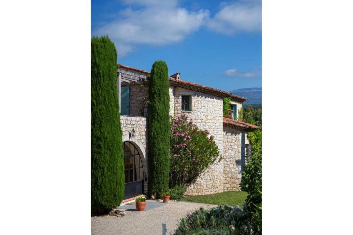 A stone house with a red tile roof and trees in front of it