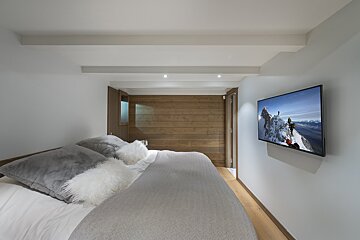 A bedroom with a flat screen tv on the wall above the bed