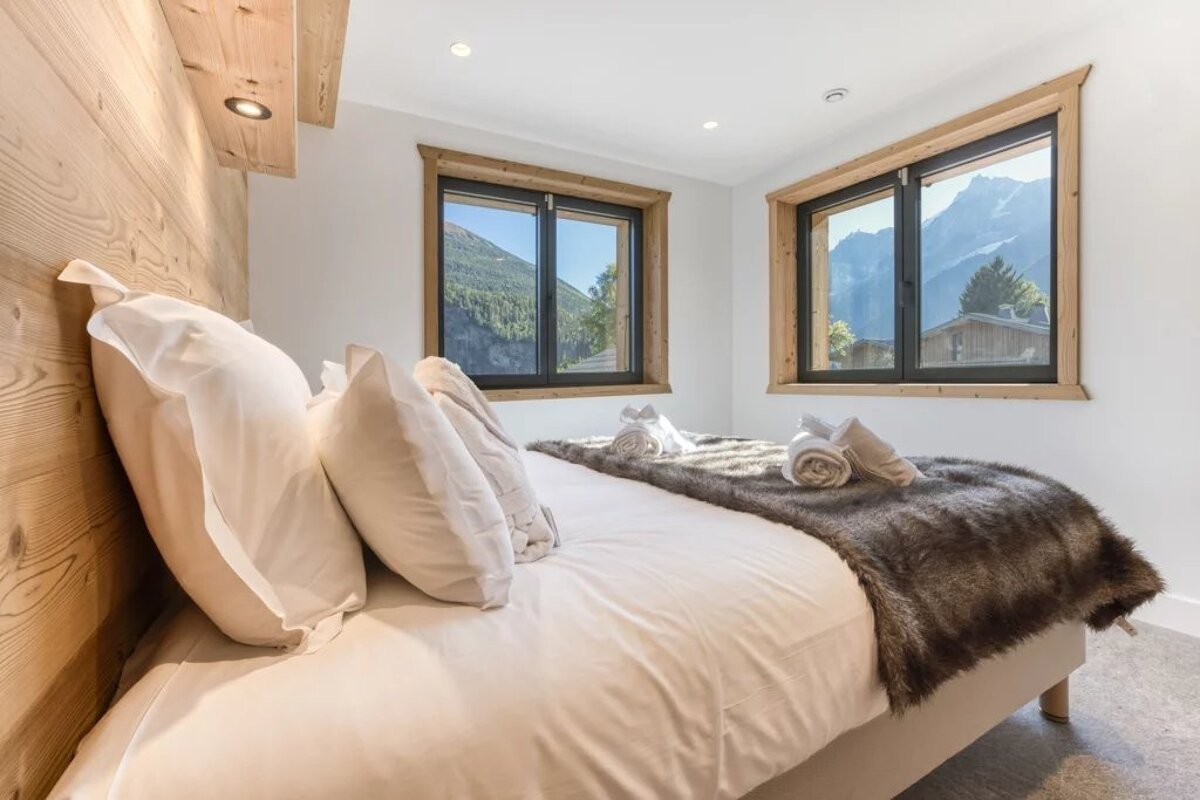 Cozy chalet bedroom with a plush bed, wooden accent wall, and windows offering a scenic mountain view.