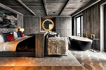 Luxurious modern suite featuring dark wood paneling, a plush bed, a chic black freestanding tub, and an illuminated mirror.