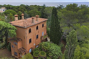 A large house with a red tiled roof is surrounded by trees