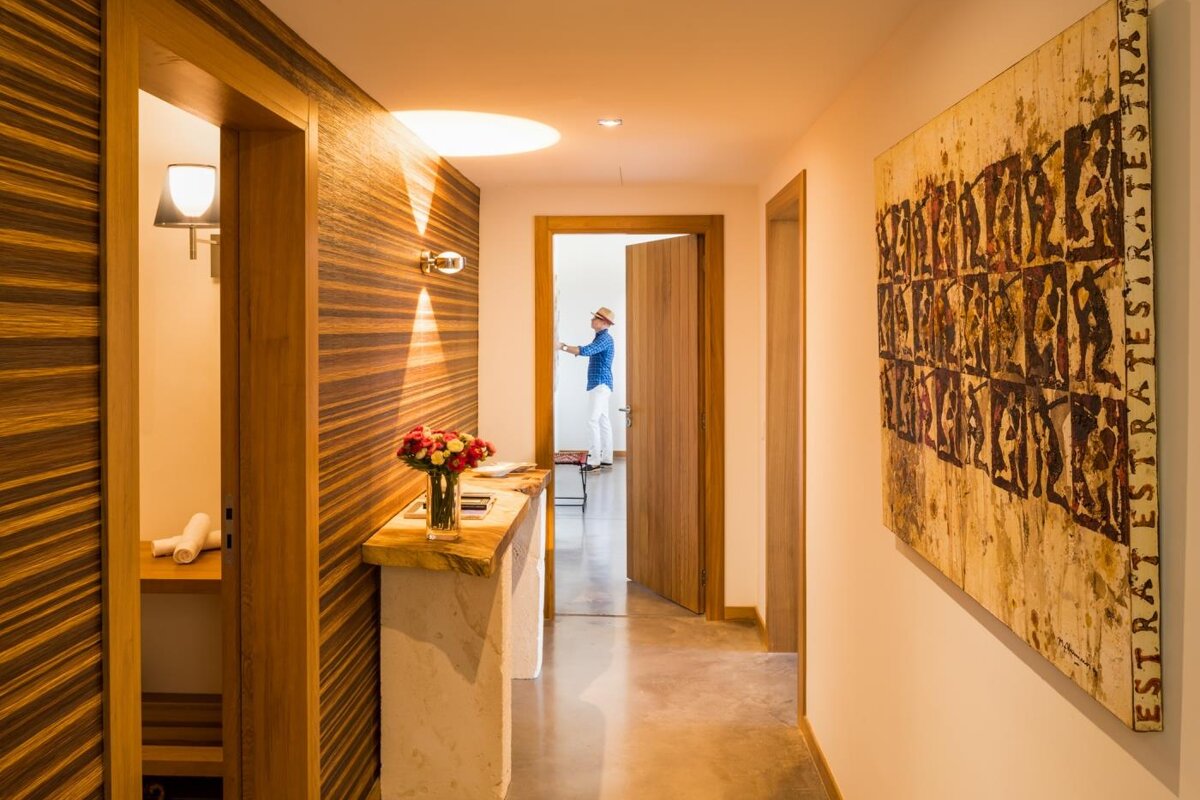 A woman in a blue shirt is standing in a hallway with a painting on the wall