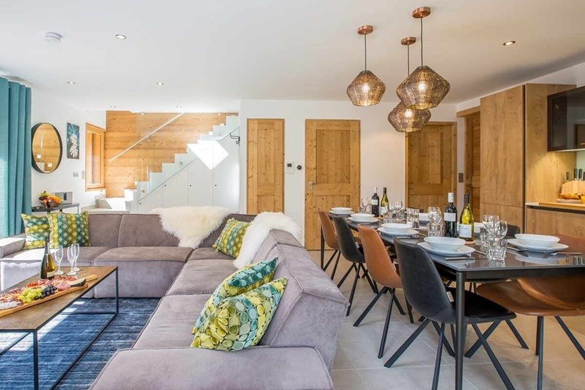 Modern open-plan living space featuring a grey sectional sofa, set dining table, wooden elements, and stylish pendant lights.