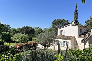 A white house with blue shutters is surrounded by trees