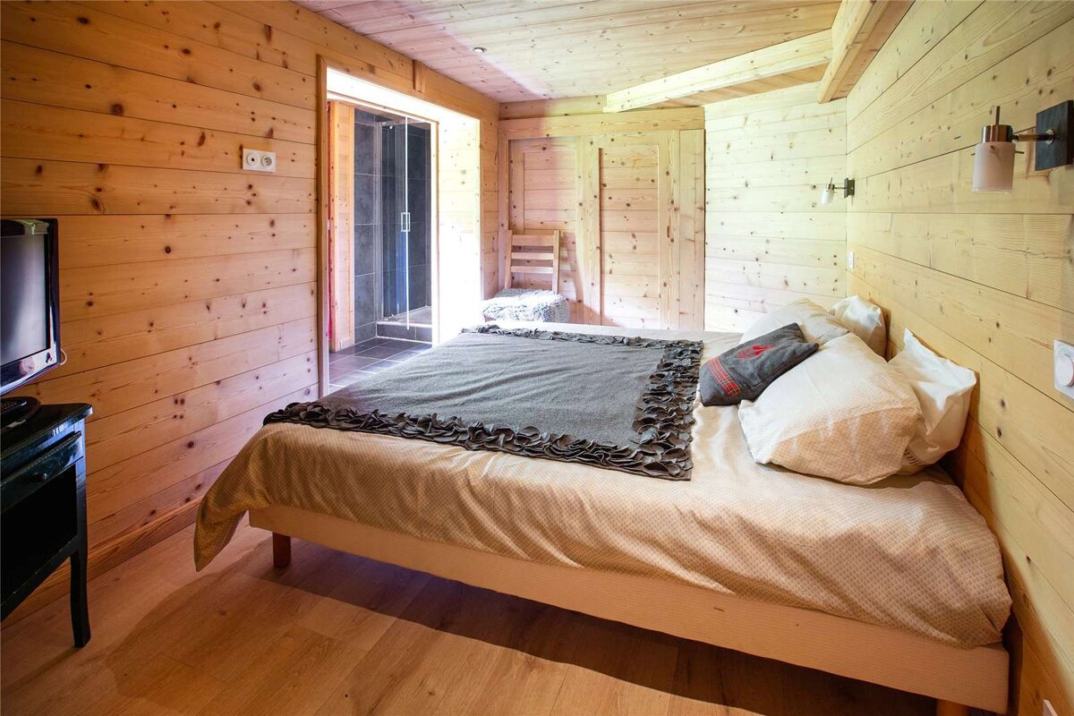 A wooden bedroom with a bed and a television