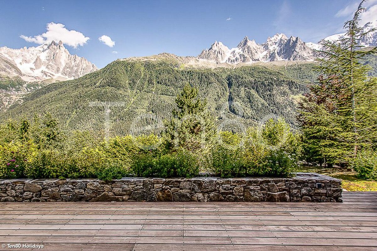 A wooden deck with a stone wall and mountains in the background