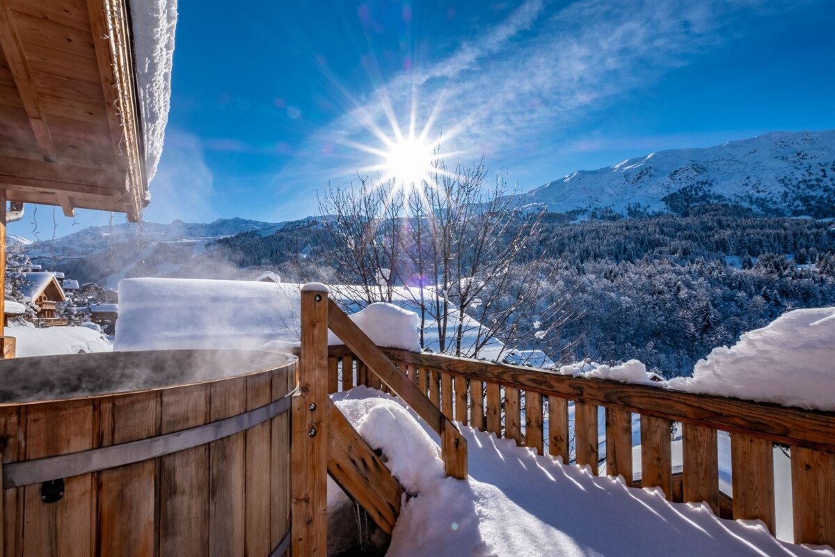 A hot tub on a snowy deck with mountains in the background