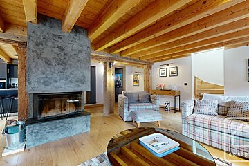 A modern rustic living room features exposed wooden beams, light wood floors, a sleek concrete fireplace, and plaid sofas/armchair.