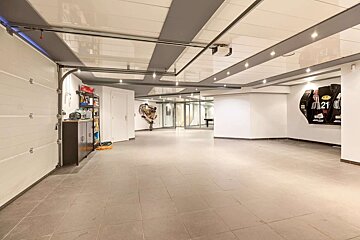 Spacious, modern garage with tiled floor, white overhead door, storage unit, sleek ceiling, and unique wall art.
