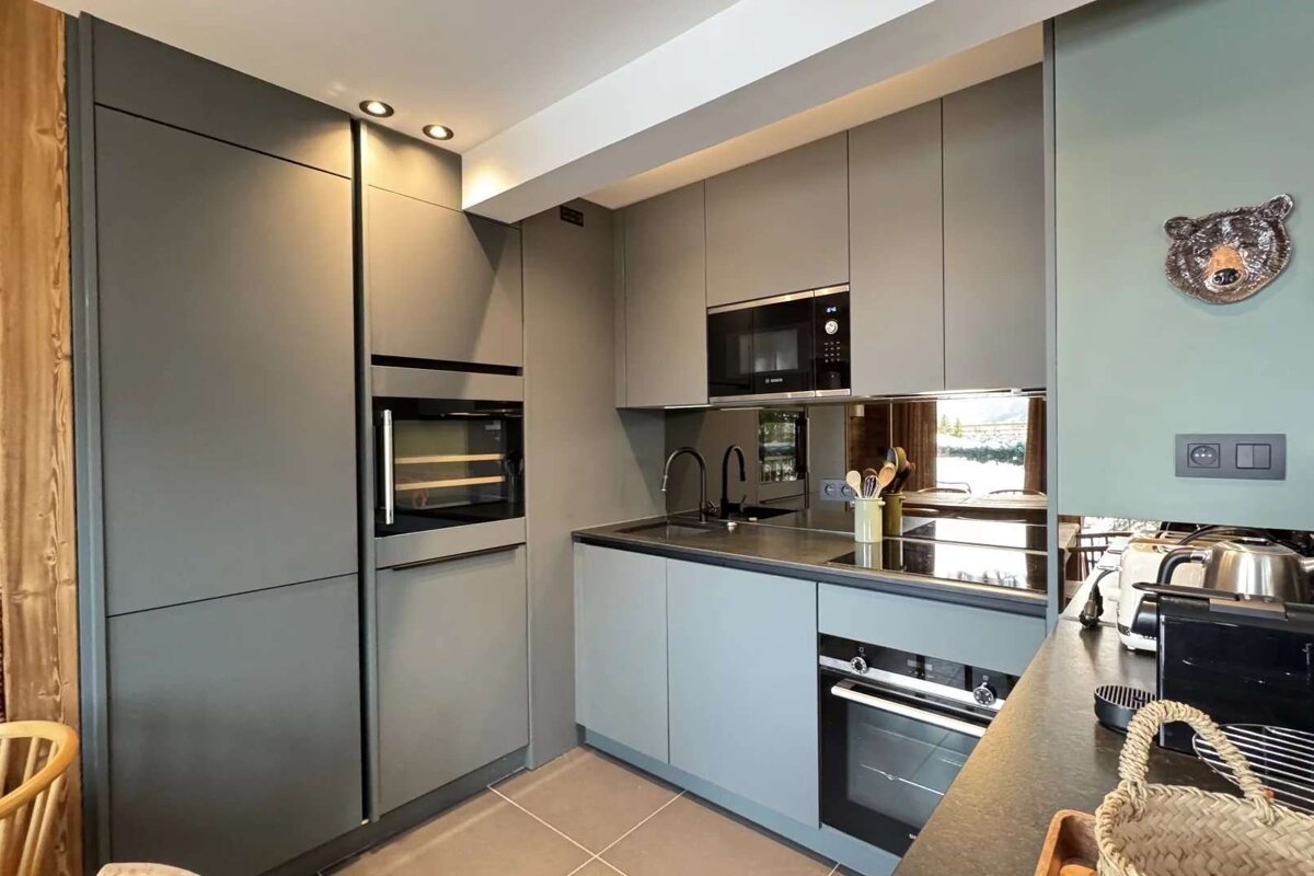 A modern gray kitchen features integrated appliances, a mirrored backsplash, and a unique bear head wall decor, blending sleek design with a rustic touch.