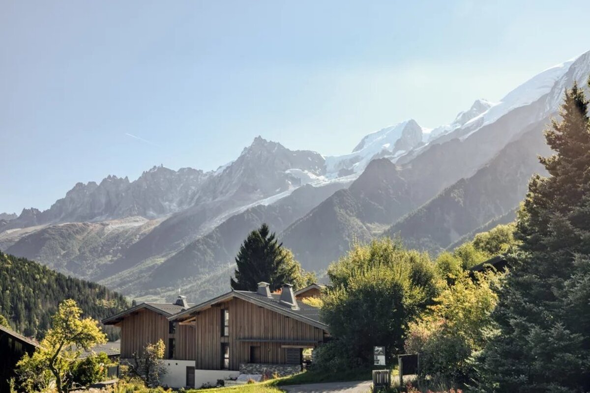 Wooden chalets in a mountain valley, with a backdrop of snow-capped alpine peaks.