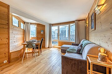 A cozy, wood-paneled living/dining room with a sofa, dining table, and large windows offering views of mountains and buildings.