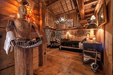 Cozy wooden cabin bedroom featuring a wooden mannequin statue serving wine in the foreground.