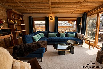 Cozy alpine chalet living room with a large blue velvet sectional, warm wooden paneling, and modern round coffee tables.