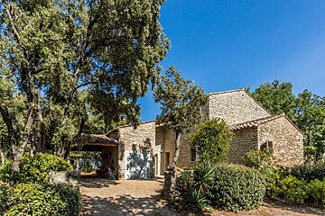 A stone house with a blue garage door is surrounded by trees