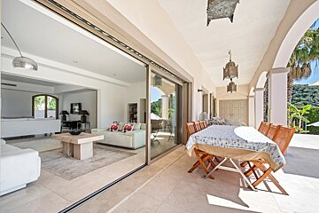 Modern villa terrace with an outdoor dining table, sliding glass doors opening to a bright, stylish indoor living room.