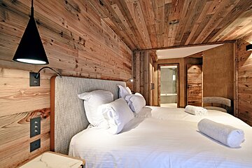 Cozy rustic bedroom with wood-paneled walls and ceiling, a bed with white linens, and a black cone pendant light.