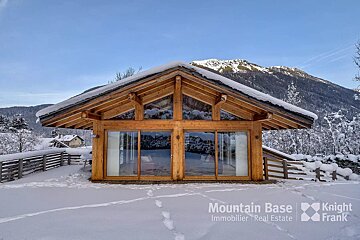 A wooden cabin with snow on the roof is owned by mountain base immobilier real estate
