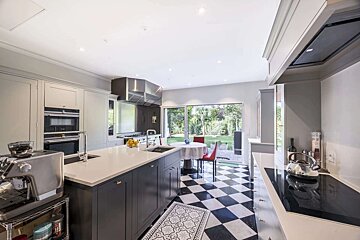 A contemporary kitchen with light grey cabinets, a large island, black and white checkered floor, and a bright view of the garden.