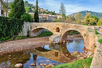 A stone bridge over a river with a village in the background