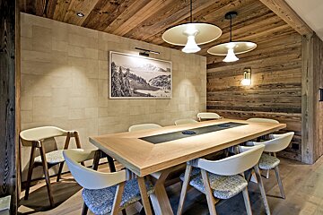 A cozy modern dining room with a long wooden table, stylish chairs, wood-paneled walls, and two elegant pendant lights.