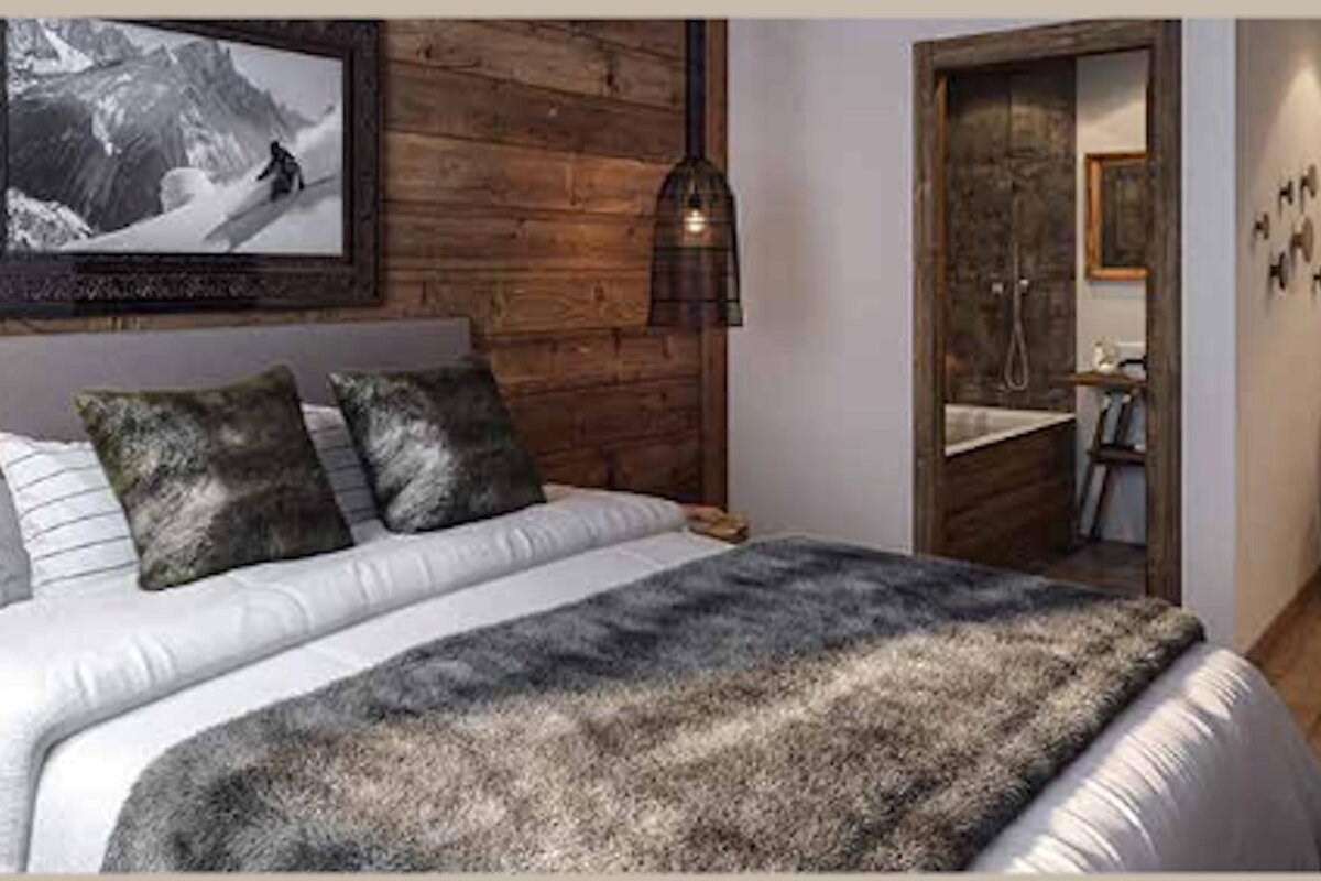 Rustic mountain-cabin-style bedroom with a wooden accent wall, furry grey throw blanket, and a doorway leading into a bathroom.