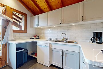 Modern L-shaped kitchen featuring white cabinets, subway tile backsplash, a stainless steel sink, wood-paneled ceiling, and a dishwasher.