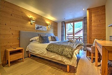 A cozy, rustic bedroom with wood-paneled walls, a bed with a furry throw, and glass doors opening to a scenic balcony.