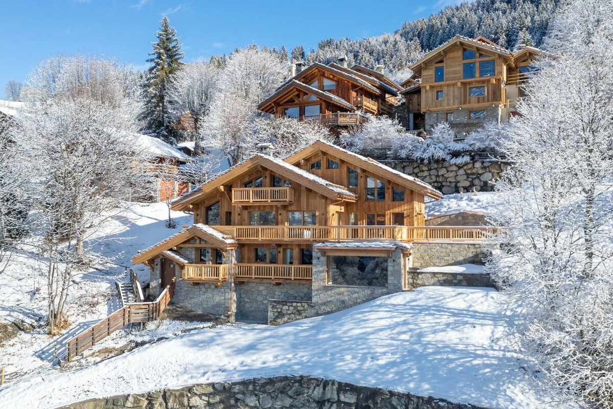 Luxurious wooden chalets nestled in a pristine, snow-covered mountain landscape under a clear blue winter sky.