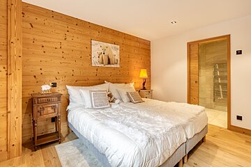 Cozy chalet-style bedroom with warm wood paneling, a plush white bed with faux fur throw, polar bear art, and an en-suite bathroom.