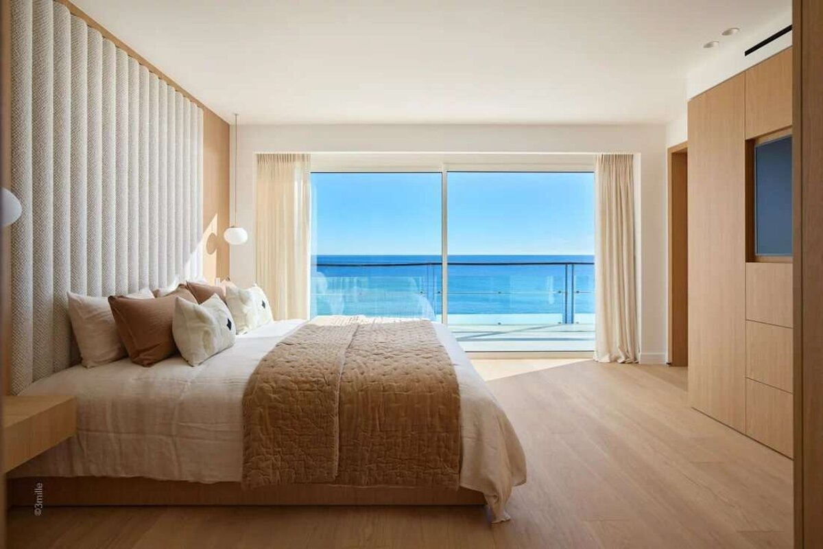 A bedroom with a large bed and a balcony overlooking the ocean