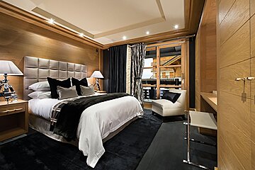 Stylish bedroom with wood paneling, a large bed with black and white bedding, a dark rug, and a window looking out at chalets.