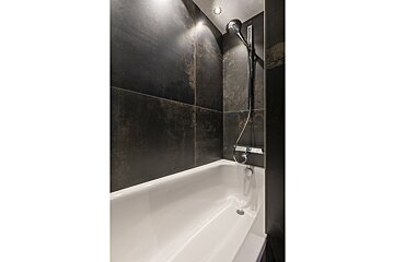 A bathtub in a bathroom with black tiles and a shower head