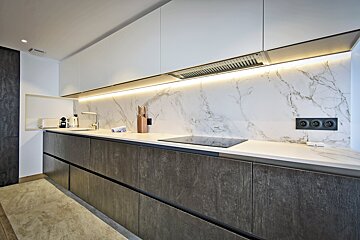 Stylish modern kitchen with white and dark textured cabinets, marble backsplash, under-cabinet lighting, induction hob, and sink.