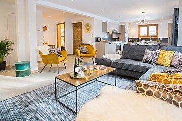 Cozy, modern open-plan living room with a gray sectional sofa, yellow armchairs, a coffee table, and a kitchen in the background.