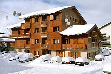 Snow covered cars are parked in front of a wooden building