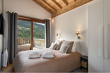 A bedroom with a large bed and a balcony overlooking the mountains