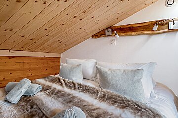 A bed with white sheets and pillows under a wooden ceiling